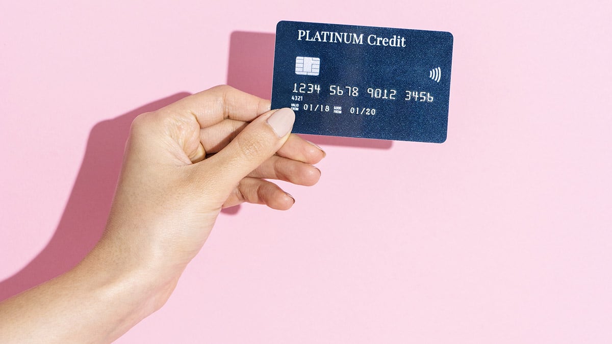 Woman holding a credit card against a pink background