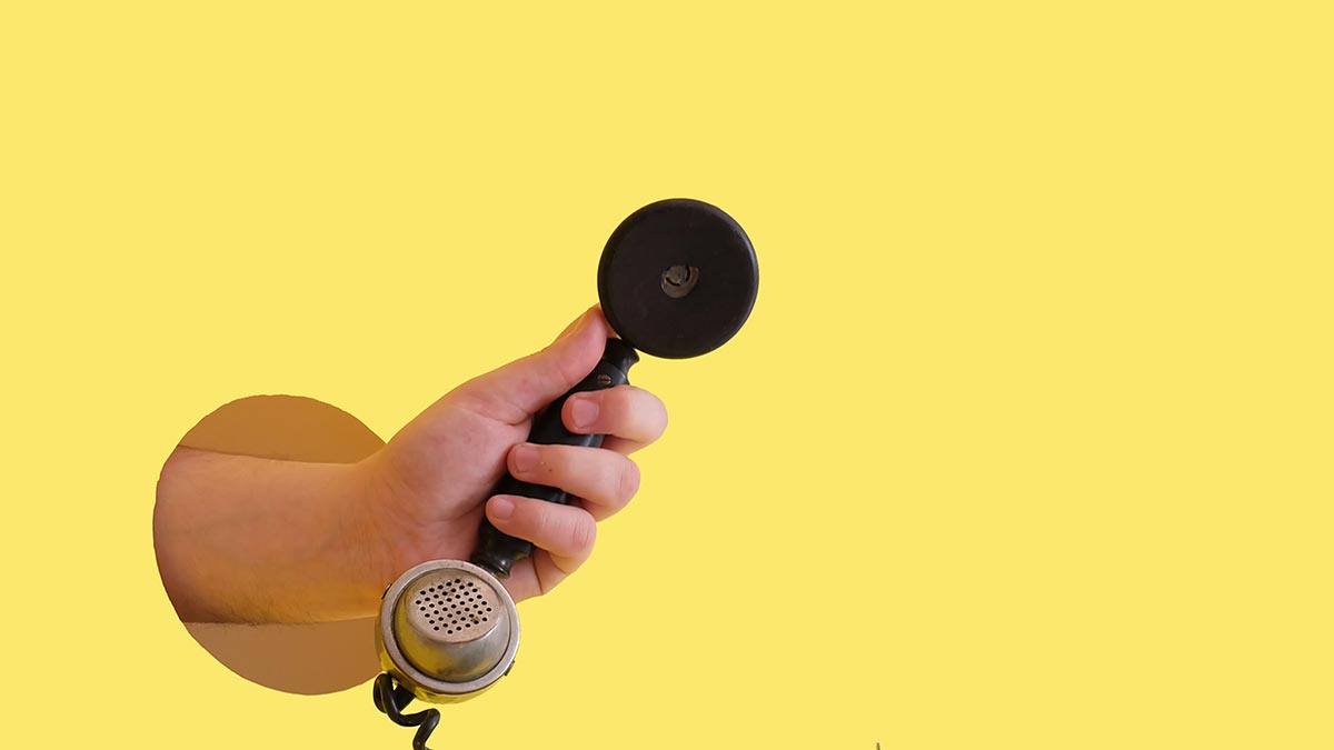 Una mano sujetando un teléfono a través de un agujero en la pared